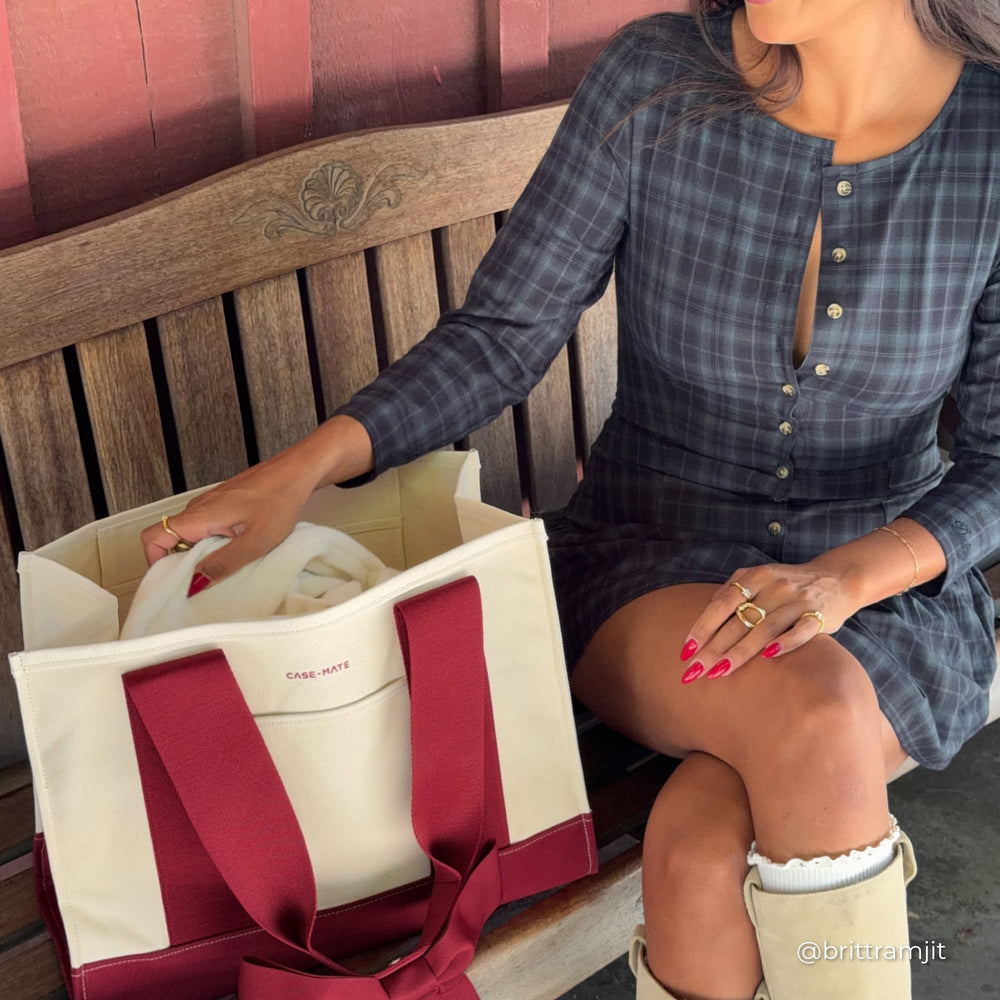 Woman sitting on an outdoor bench with canvas tote on the bench open next to her.
#color_cranberry bow