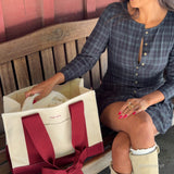 Woman sitting on an outdoor bench with canvas tote on the bench open next to her.
#color_cranberry bow