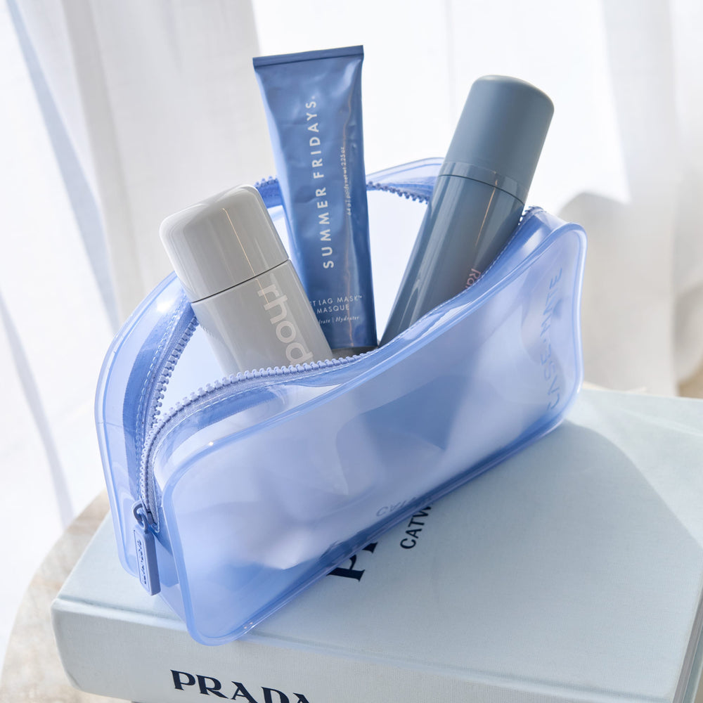 Blue cosmetic bag with skincare products on a Prada book