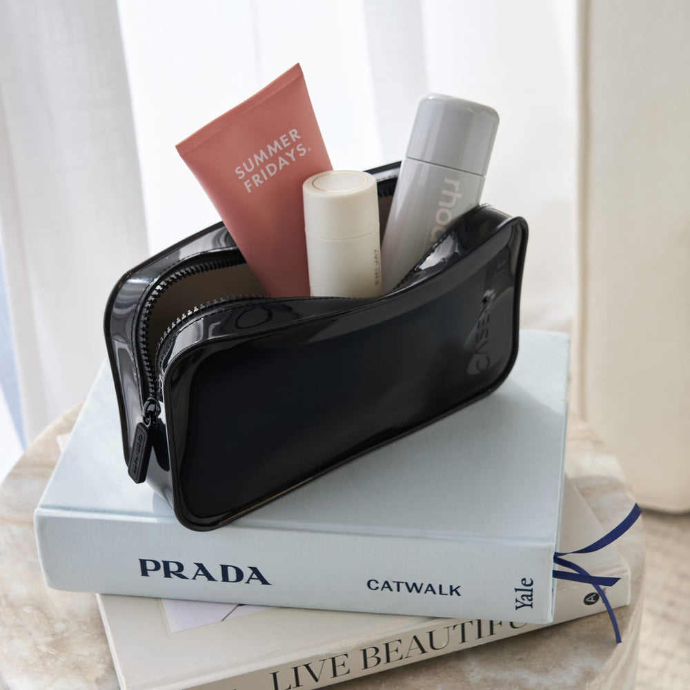 A glossy black cosmetic pouch filled with travel-sized toiletries