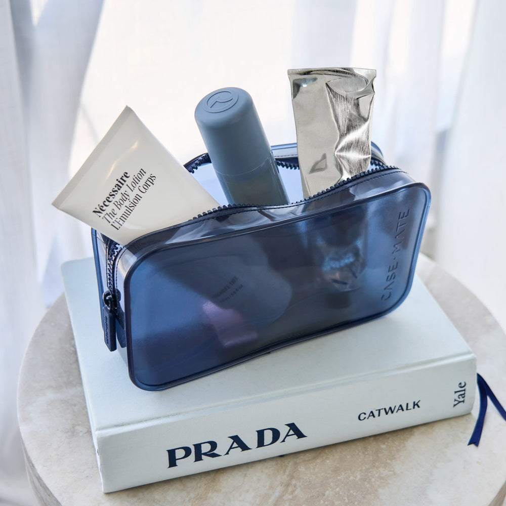 A translucent navy blue cosmetic pouch filled with skincare items, displayed on top of a white Prada book.