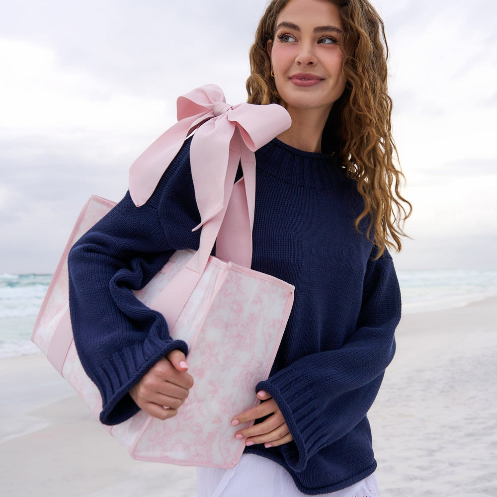 Woman holding a large pink gift bag with a bow on a beach