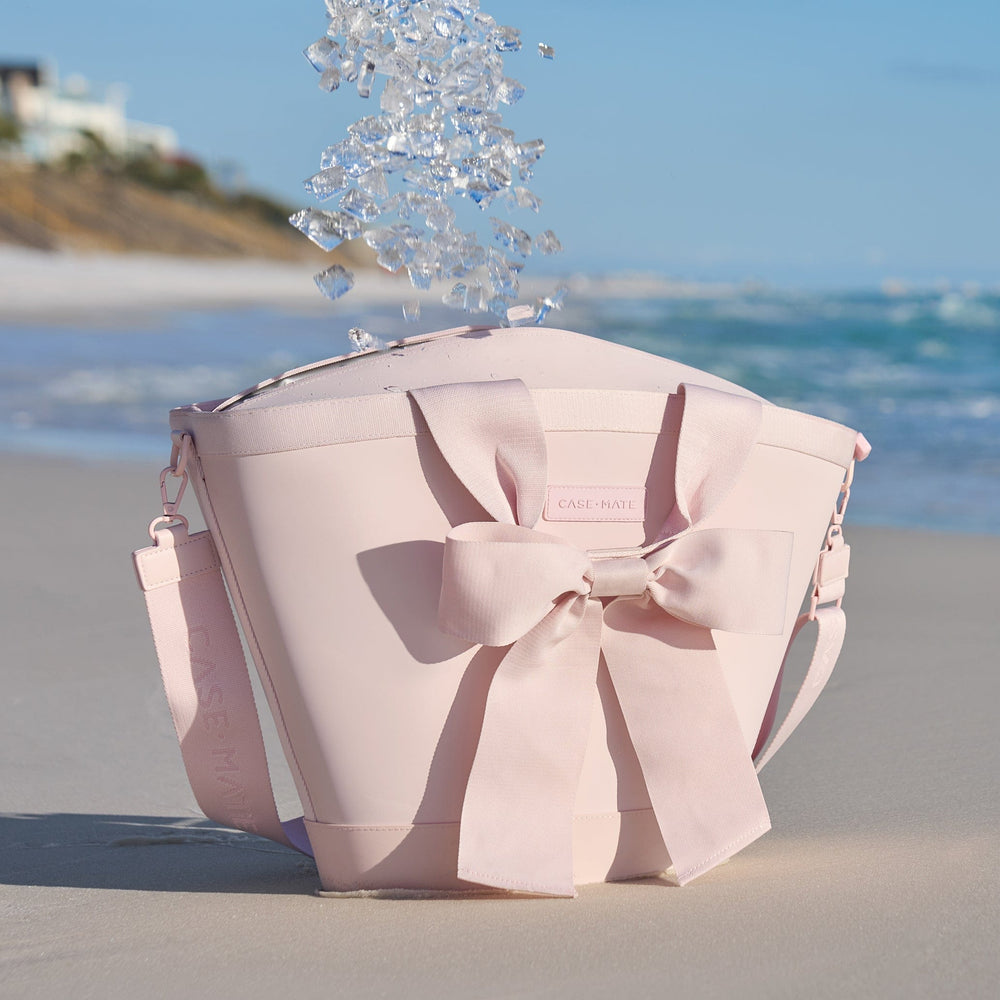 Ice cubes falling into a pink cooler with a large bow on a sandy beach with ocean and clear sky in the background
#color_ballet pink bow