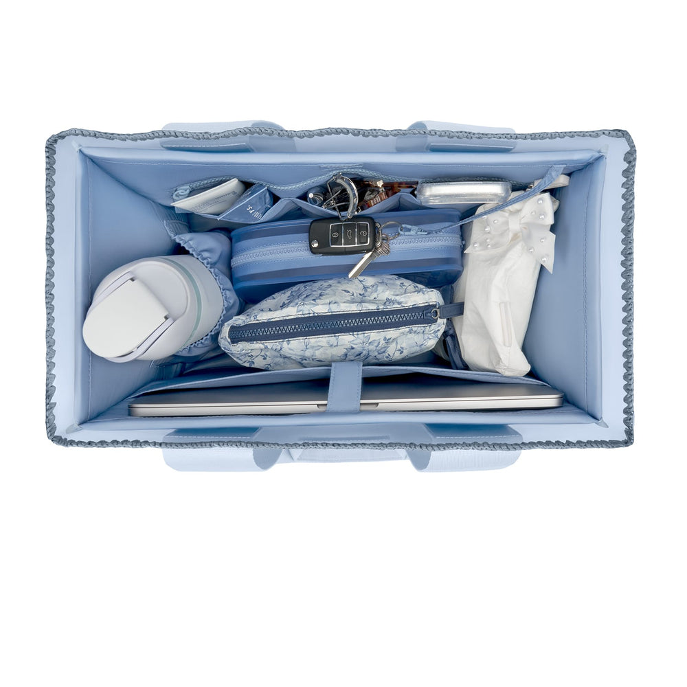 Top-down view of a light blue organizer bag filled with travel accessories, including a laptop sleeve, wallet, pouch, and a white tumbler, on a white background.

#color_carolina blue