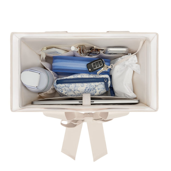 An overhead view of a cream-colored organizer box or bag filled with travel accessories, including a blue floral zip pouch, a blue striped pouch, a white drawstring bag, and a silver laptop sleeve, on a white background.

#color_french vanilla 