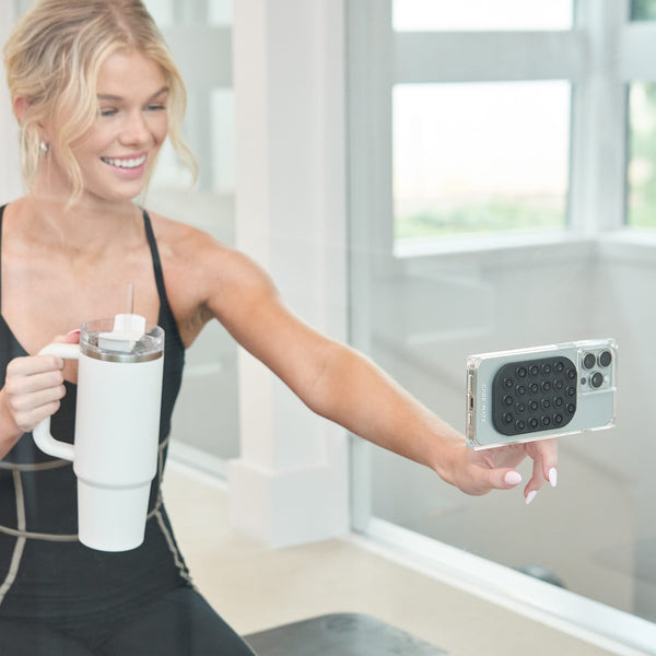 Woman holding a white mug and a smartphone with a clear case in an indoor setting.
#color_midnight black