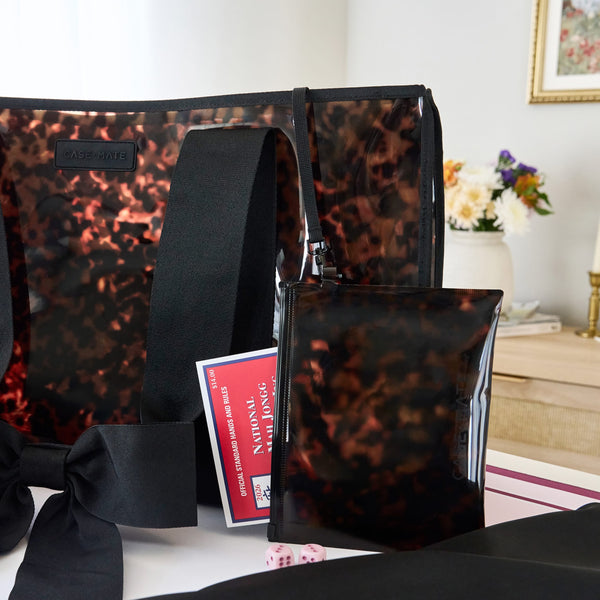 A clear tote bag with a black tortoiseshell pattern, black shoulder strap, and matching black pouch, displayed on a table with a mahjong card in a home interior setting.

#color_tortoiseshell bow