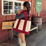 Woman in cabin-like setting with canvas tote on her shoulder. 

#color_cranberry bow
