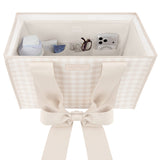 A square fabric storage organizer bin with a beige and white gingham pattern, featuring wide cream-colored shoulder straps tied into a large bow at the front. The open top of the bin is shown holding various small personal items like a phone, glasses, and a small bottle.

#color_french vanilla 