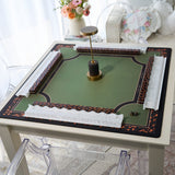 A square mahjong table mat with a green center, black and orange decorative borders, white textured corner guards, and a central gold-and-black stand, shown on a white table in a softly lit room.
#color_ivory pearl
