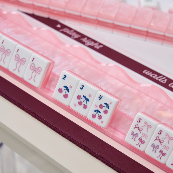 Pink and white mahjong tiles with cherry and bow designs, arranged in a clear plastic case with a dark burgundy zipper and decorative ribbon.
#color_ballet pink pearl edition