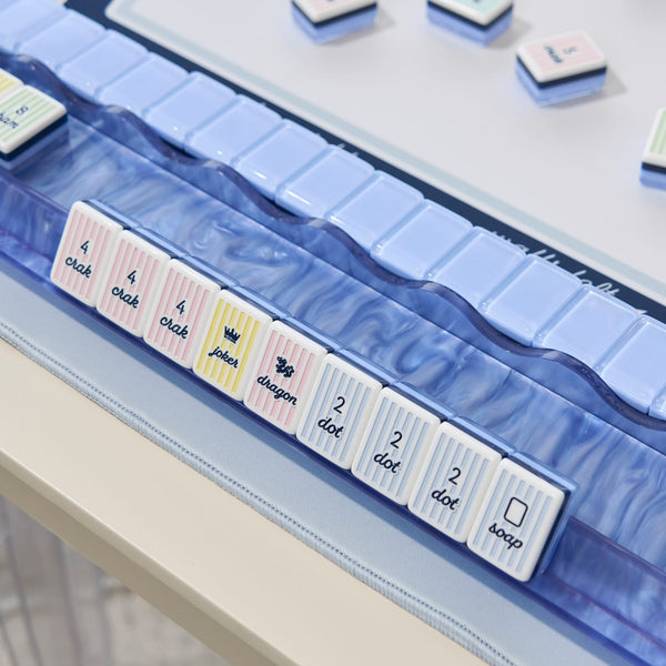 A close-up of a translucent blue acrylic organizer tray holding several pastel-colored playing card tiles with printed card faces
#color_cabana stripe edition