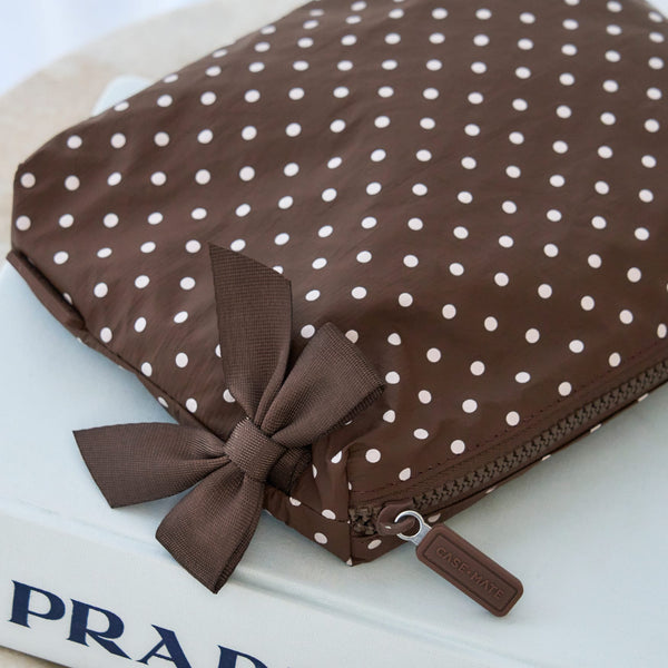 A brown zippered pouch with a white polka dot pattern and a matching brown ribbon bow, resting on a white book.
#color_espresso polka dot bow
