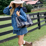 A woman outdoors wearing a denim shirt and skirt outfit, a wide-brim hat, and carrying a large black tote bag with a gray marbled pattern. She is standing in front of a black wooden fence on a grassy lawn with a house in the background.

#color_navy bandana bow