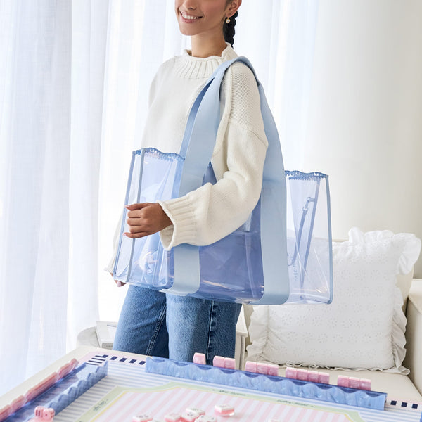 A woman wearing a cream knit sweater and blue jeans carries a large, clear plastic tote bag with light blue straps in a bright, modern room.

#color_carolina blue crochet wave