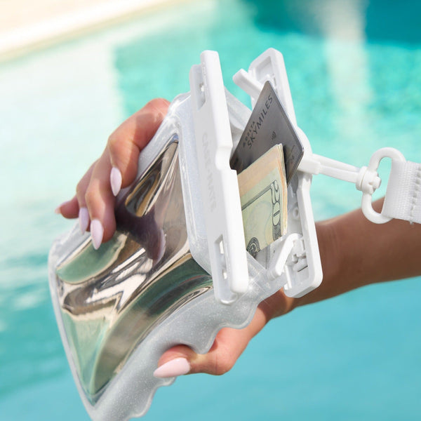Hand holding a clear plastic wallet with money and a card against a blurred pool background #color_ivory twinkle