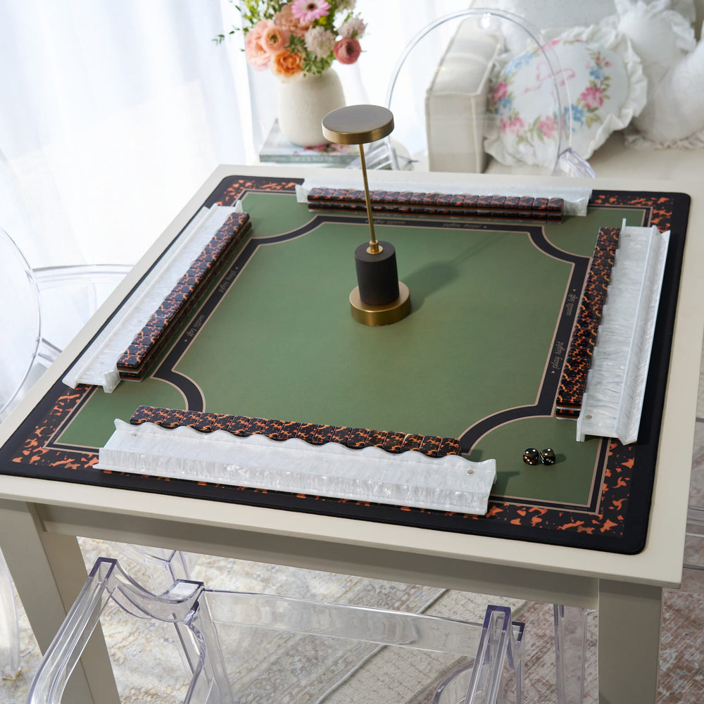 A square mahjong table mat with a green center, black and orange decorative borders, white textured corner guards, and a central gold-and-black stand, shown on a white table in a softly lit room.
#color_classic tortoiseshell