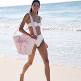 Woman in a white bikini with a pink bow cooler bag on a beach #color_ballet pink bow