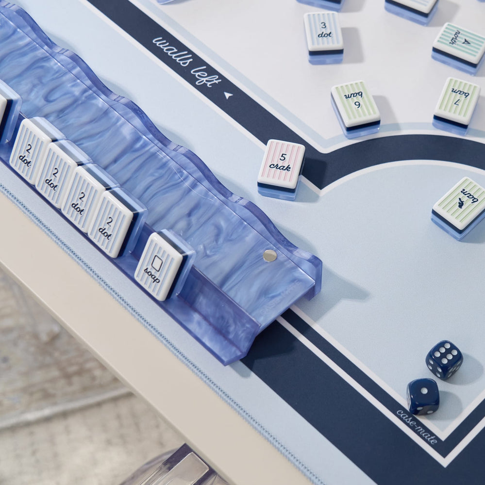 A close-up of a board game setup on a light tabletop, showing a translucent blue marble dice tray, white numbered tiles with blue and pink striped borders, and blue dice.
#color_carolina blue pearl