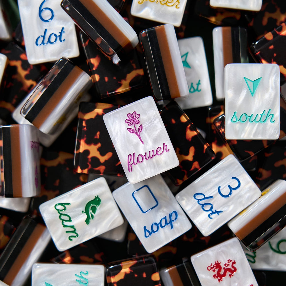 A close-up pile of rectangular nail tips with mother-of-pearl white fronts featuring various colorful script words and symbols, layered over leopard-print and striped black, brown, and white tips.
#color_tortoiseshell pearl edition
