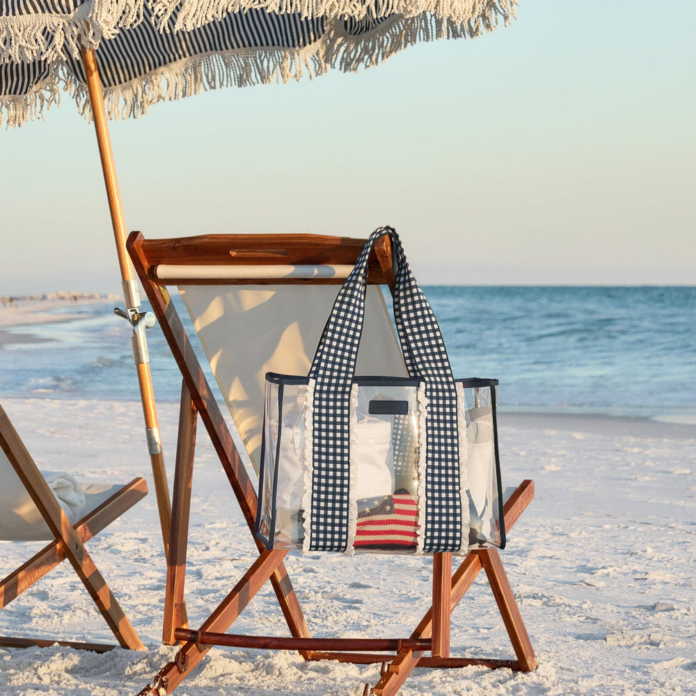Beach chair with striped cover and a tote bag hanging on corner of chair on a sandy beach with ocean view 

#color_Navy Gingham