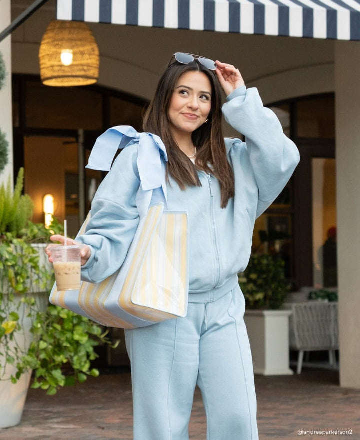 Girl standing outside a cafe in baby blue sweatsuit and Cabana Stripe Bow Jelly Tote 