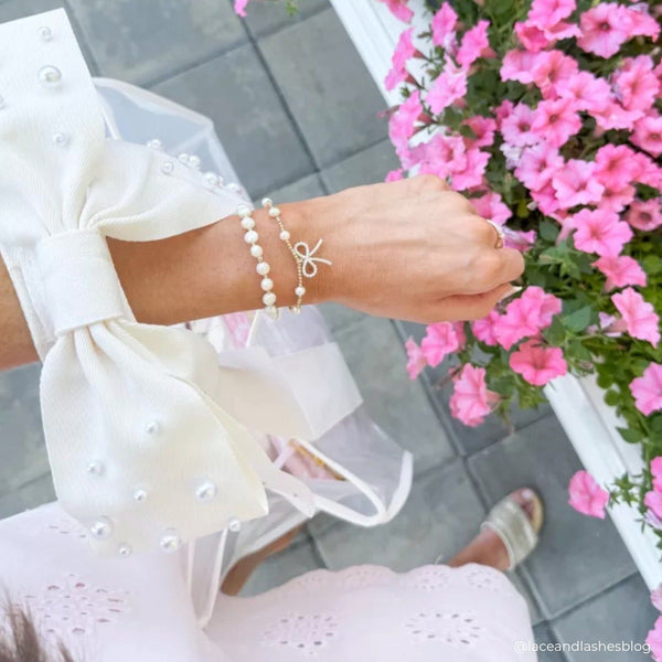 Person wearing a pearl bracelet with pink flowers in the background
#color_ivory pearl bow
