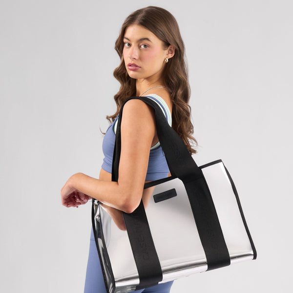 Woman carrying a clear tote bag with black straps on a gray background
#color_silver chrome
