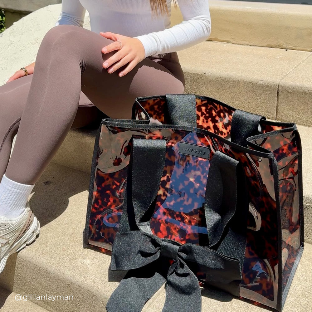 Woman sitting on steps outside with jelly tote next to her on the steps. 
#color_tortoiseshell bow