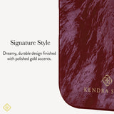 A close-up of a textured burgundy pouch or case with rounded corners, featuring a gold KENDRA SCOTT logo and text that reads 'Signature Style' and ' Dreamy, durable design finished with polished gold accents.'
#color_cherry lacquer pearl