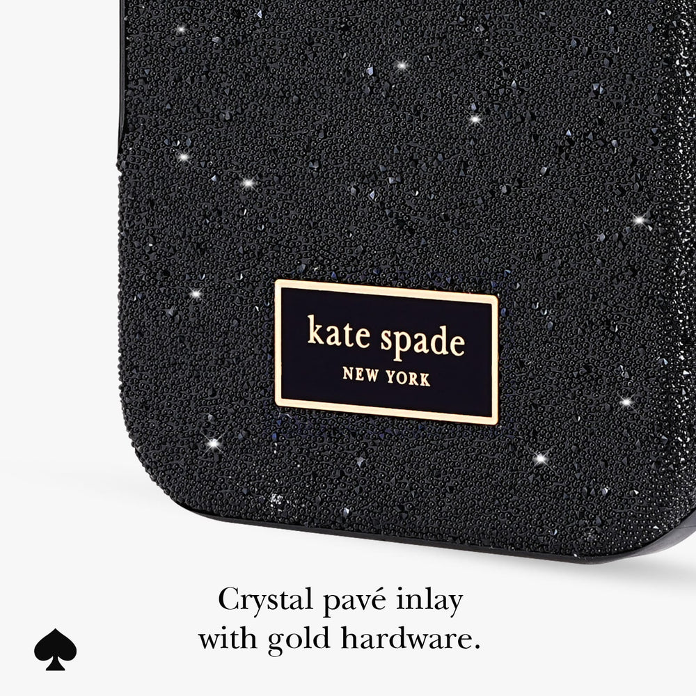 Close-up of a black sparkly crystal-covered phone case with a gold-bordered 'kate spade NEW YORK' logo patch. Text below reads 'Crystal pavé inlay with gold hardware.
#color_crystal pavé