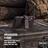 Black Pelican rugged phone case with an integrated vertical stand, shown outdoors on a metal surface with a blurred natural background. White text on the image reads 'INTEGRATED STAND' and 'PROP IT UP FOR CALLS AND DIRECTIONS WHILE ON THE JOB'.

#color_shield carbon