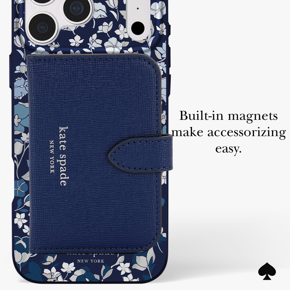 A navy blue Kate Spade New York phone case with a floral pattern border and a large textured magnetic wallet card holder on the back. The text on the right reads 'Built-in magnets make accessorizing easy.
#color_flowerbed navy
