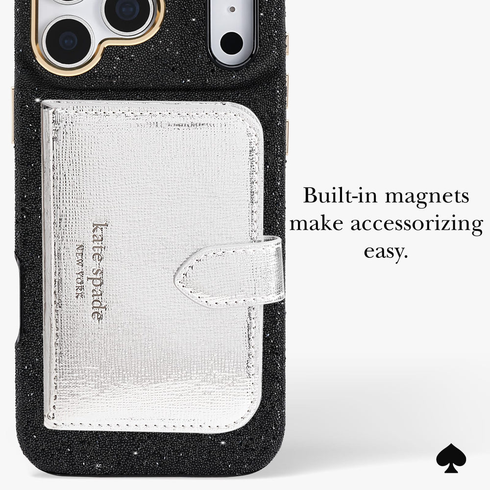 A close-up of a black glitter phone case with a built-in silver textured card holder pocket and a small strap, shown on a light gray background with text reading 'Built-in magnets make accessorizing easy.' A Kate Spade New York logo is visible on the card holder, and a black spade icon appears in the lower right corner.
#color_crystal pavé