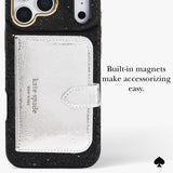 A close-up of a black glitter phone case with a built-in silver textured card holder pocket and a small strap, shown on a light gray background with text reading 'Built-in magnets make accessorizing easy.' A Kate Spade New York logo is visible on the card holder, and a black spade icon appears in the lower right corner.
#color_crystal pavé