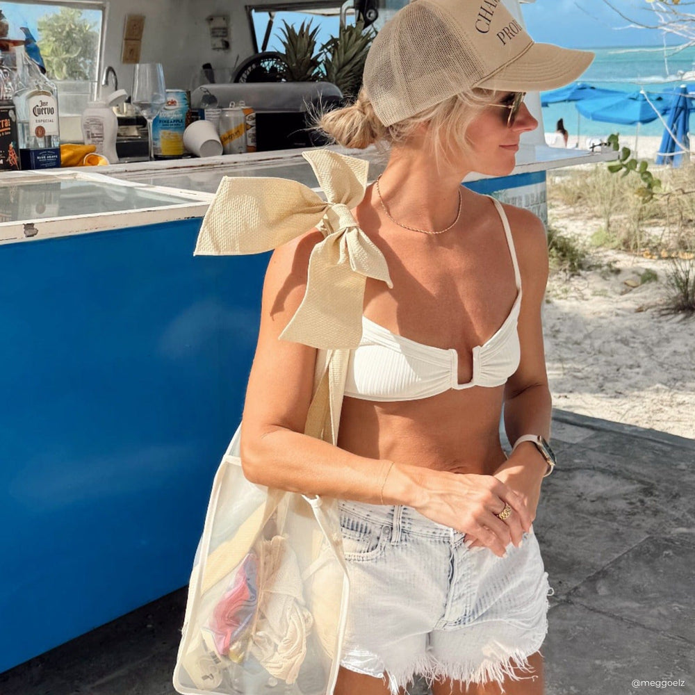 Woman in a white bikini and shorts standing on a boat with a beach in the background #color_raffia bow