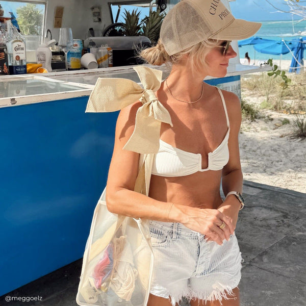 Woman in a white bikini and shorts with a large beige bow, standing on a boat.
#color_raffia bow
