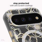 A close-up of a smartphone case with a black background and large silver and gold floral line-art pattern. The image includes text at the top reading 'stay protected with anti-scratch coatings' and shows part of the phone camera module through the case.