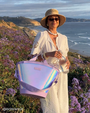 Woman standing on the coast with purple flowers behind her while she holds Soap Bubble Cooler Tote on her arm