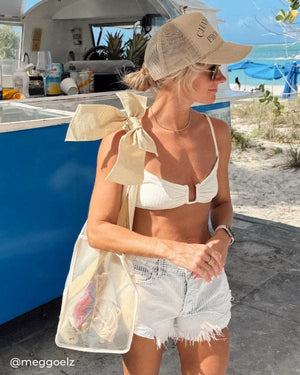 Girl by beach bar in a bikini top and shorts with Ecru Raffia Bow Jelly Tote 