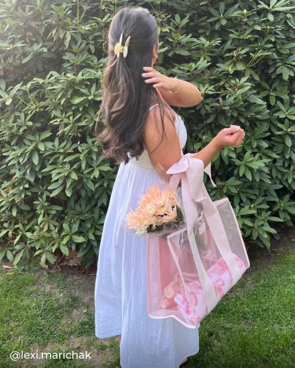 Woman standing outside throwing her hair over her shoulder in white dress holding Ballet Pink Jelly Tote