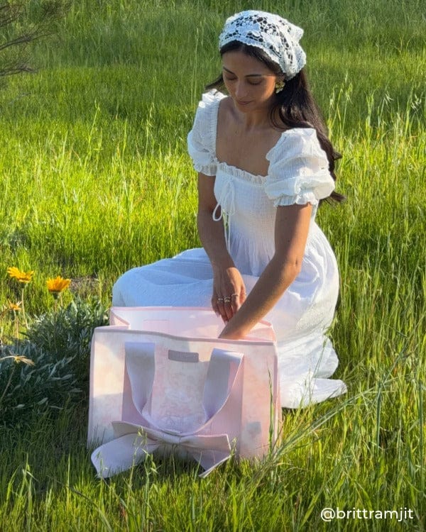Woman sitting in the grass grabbing something out of her Afternoon Rose Bow Jelly Tote