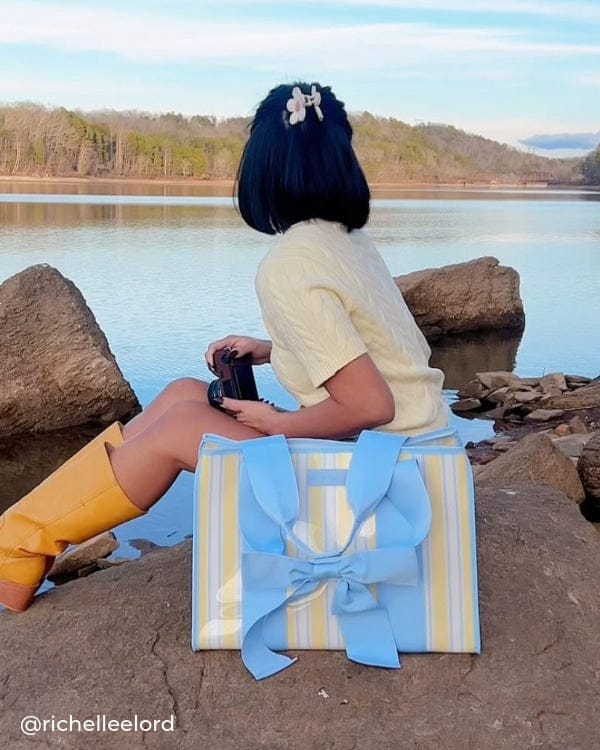 Girl sitting by a lake outdoors looking at the water with Cabana Stripe Bow Jelly Tote 
