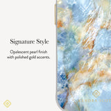 A close-up of a phone case with a marbled opalescent finish in shades of light blue, white, and soft gold, shown next to text reading 'Signature Style' and 'Opalescent pearl finish with polished gold accents.' A small 'KENDRA SCOTT' logo appears near the bottom right of the case.
