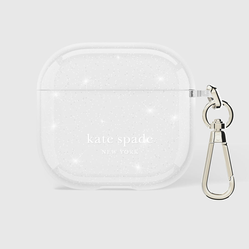 A clear, glittery AirPods case with 'kate spade NEW YORK' printed in white on the front, featuring a silver metal carabiner clip on the side, set against a light gray background.
