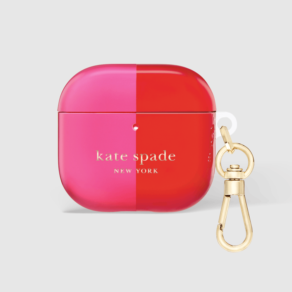 A glossy split-color AirPods case by Kate Spade New York, featuring a vibrant pink left half and a bright red right half, with a gold-tone carabiner clipped to the side, set against a light gray background.