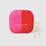 A glossy split-color AirPods case by Kate Spade New York, featuring a vibrant pink left half and a bright red right half, with a gold-tone carabiner clipped to the side, set against a light gray background.