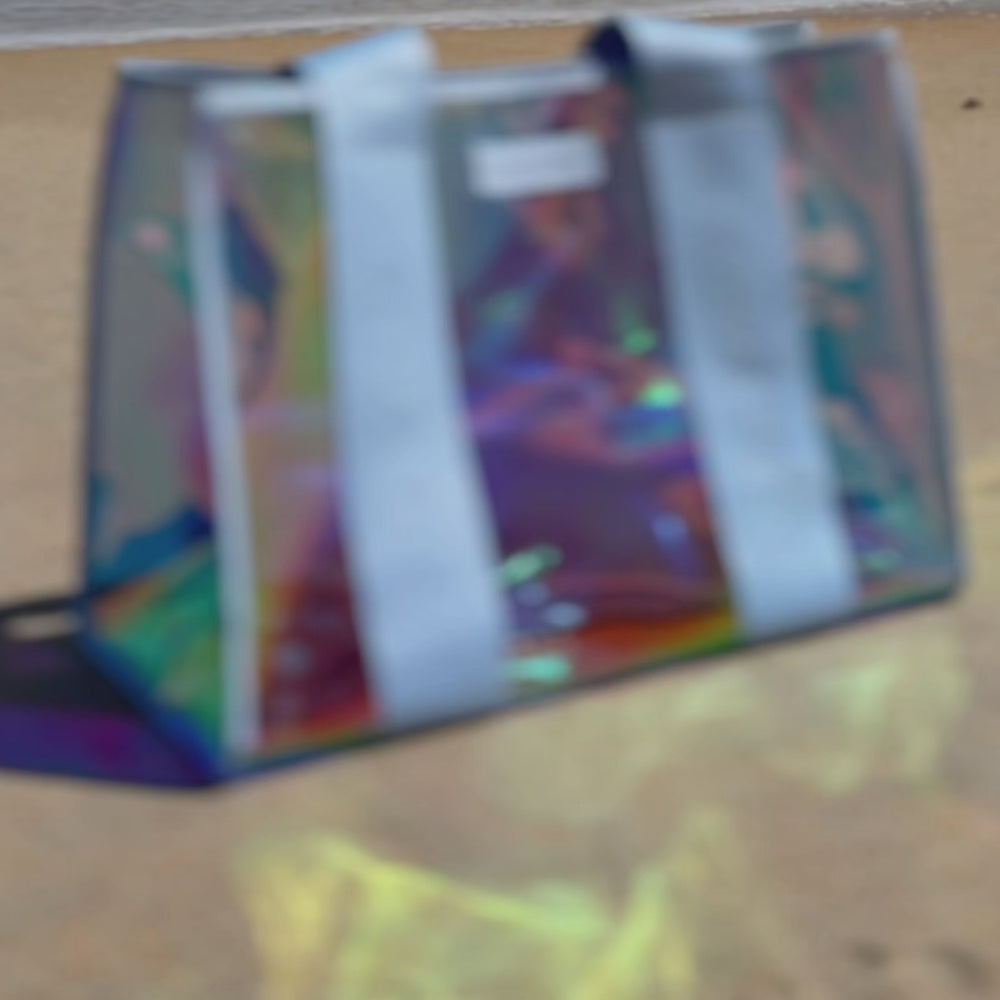 Woman packing jelly tote with various items while sitting on a towel on a beach
#color_carolina blue iridescent