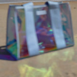 Woman packing jelly tote with various items while sitting on a towel on a beach
#color_carolina blue iridescent