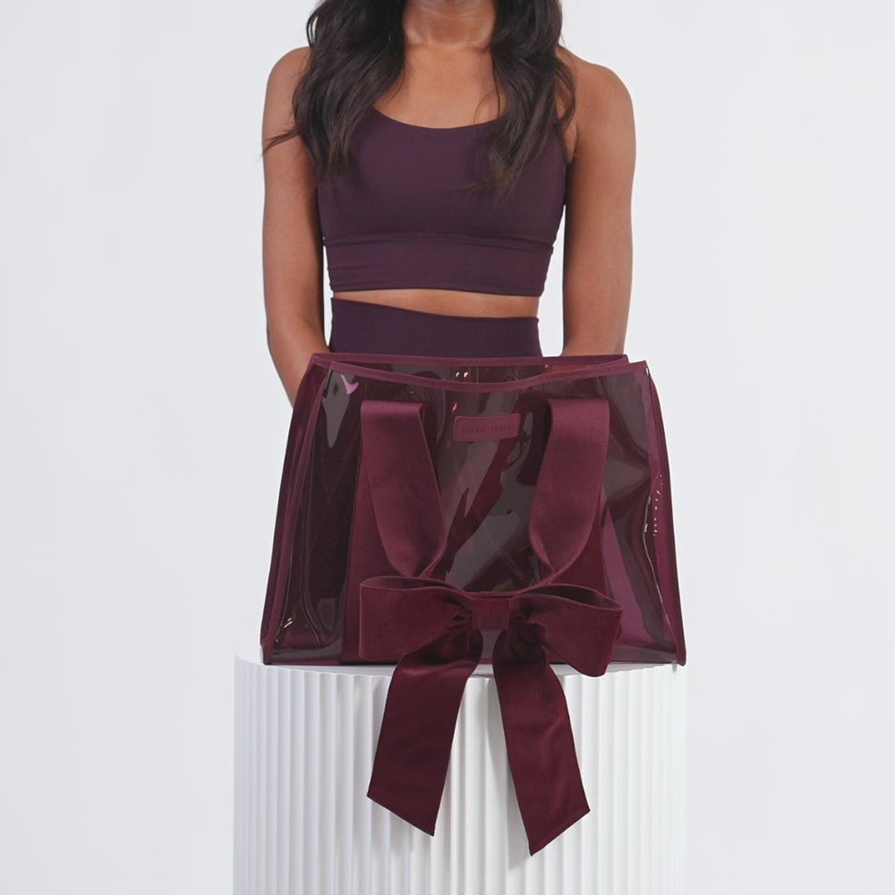 Woman in a studio setting packing her tote bag with various items and then walking off screen. #color_holiday edition red velvet bow
